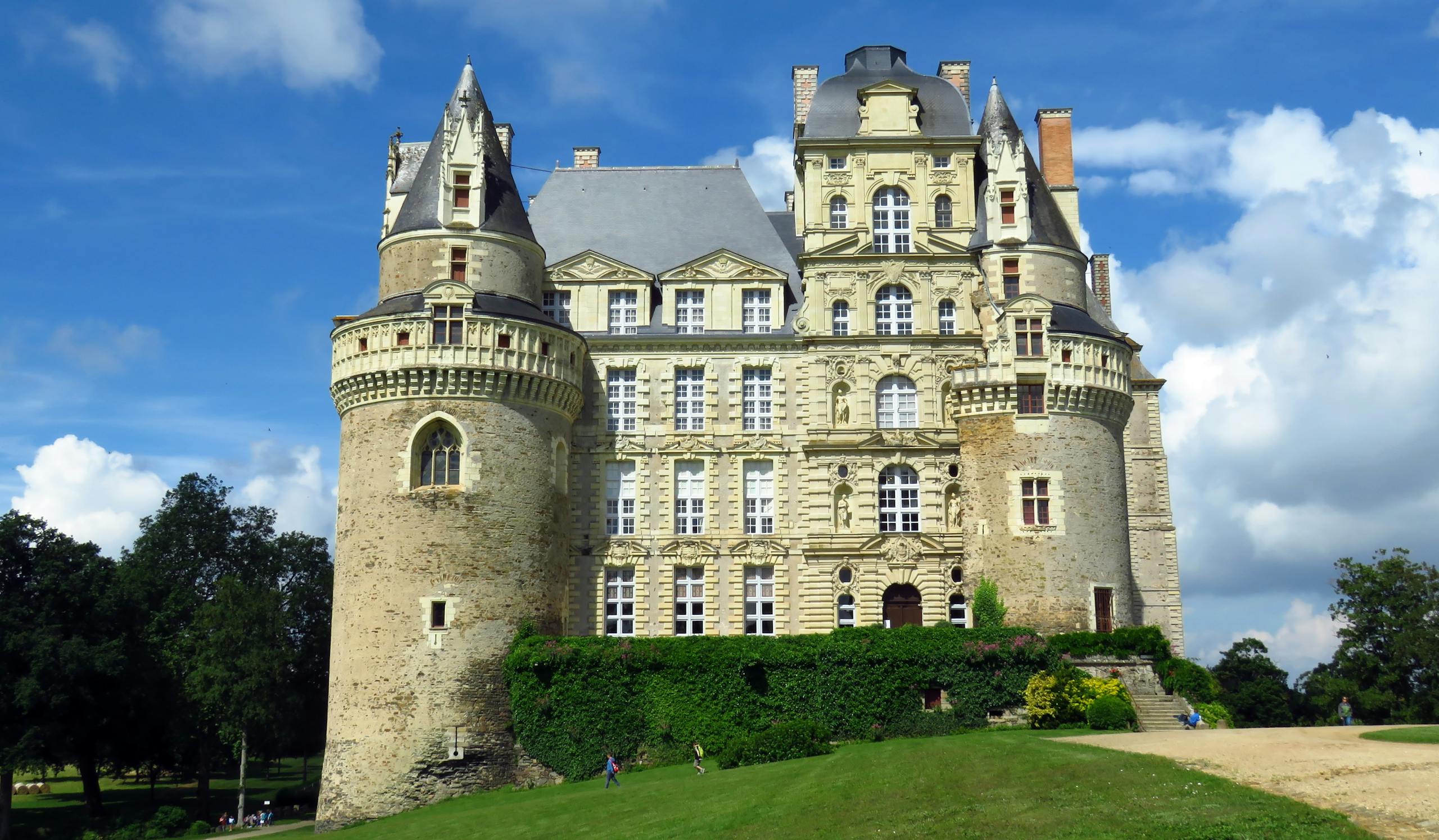 A sunlit view of the medieval Brissac Castle with blue sky and lush green surroundings.