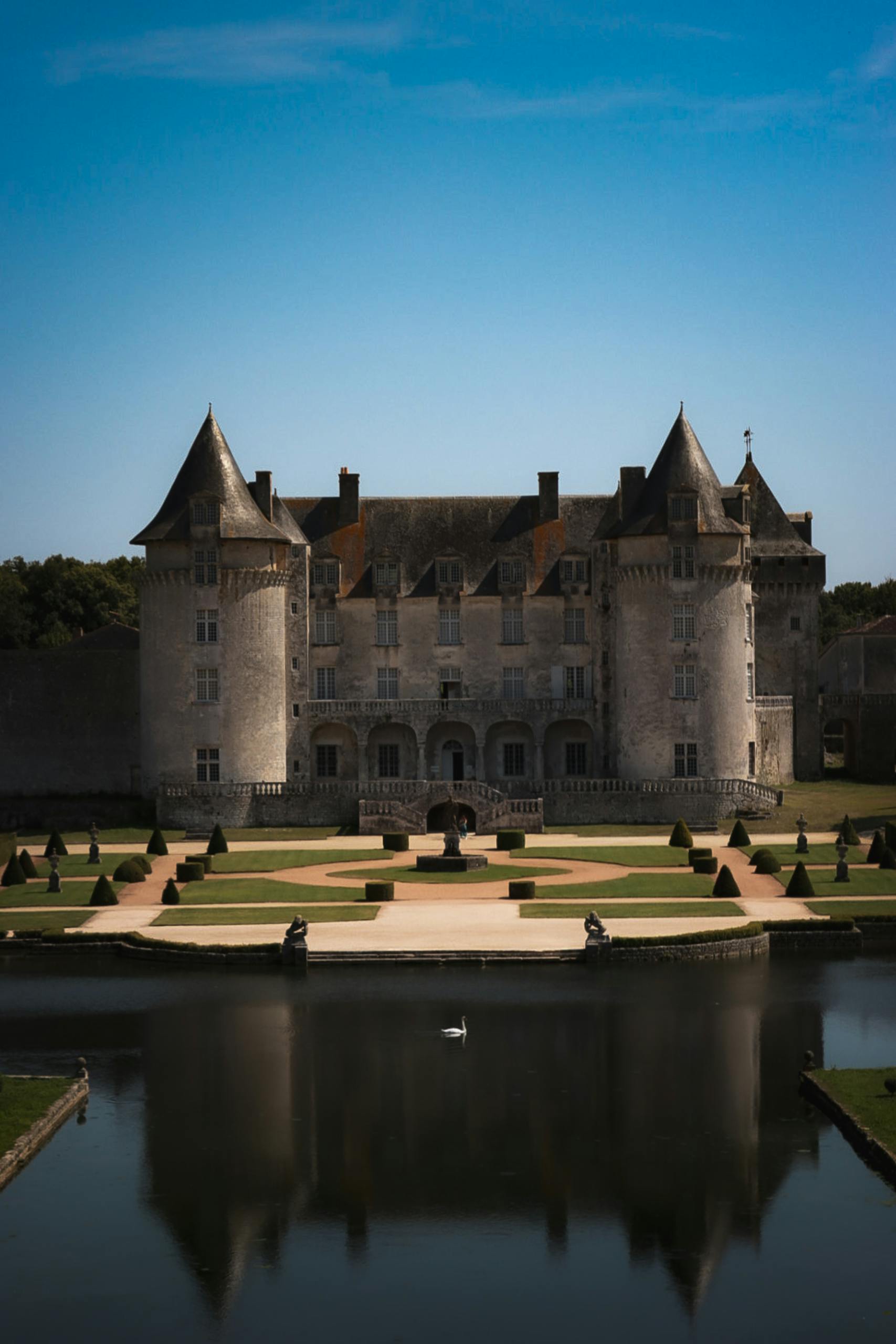 Majestic French chateau with a symmetrical garden and swan on a tranquil pond.