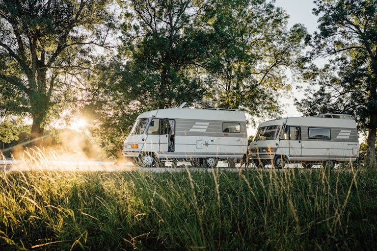 Two vintage camper vans parked in a scenic field during sunrise in Ormes, France, surrounded by nature.